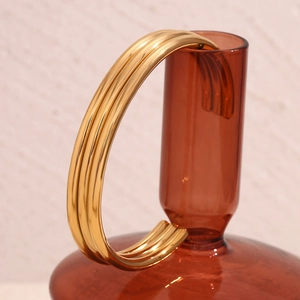 Detail of three-layer gold plated stainless steel bangle on a brown glass bottle
