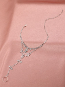 Detailed macro view of silver rhinestone tassel anklet with ring on pink silk background