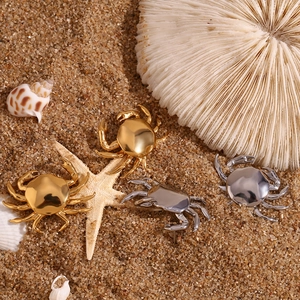 Close-up of gold and silver crab earrings on a sandy beach with seashells and starfish