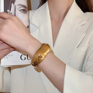 Close-up of a wide polished gold metal cuff bracelet with irregular wavy minimalist design