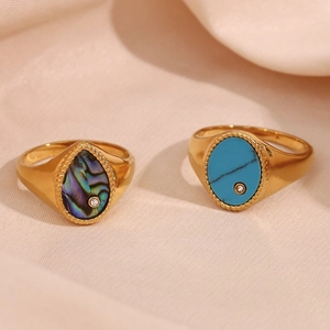 Close-up of gold rings with turquoise and abalone shell on soft silk fabric