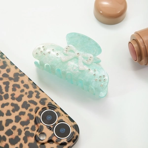 Detail of mint green acetate hair claw clip with white bow and sparkling rhinestones