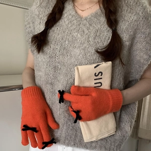 Detail view of orange knitted gloves featuring black bow decorations and soft winter texture