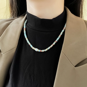 Close-up of colorful beaded pearl necklace with a central blue oval bead on a model
