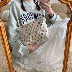 Detail shot of a floral cotton pouch with brand tag held by a model in home setting