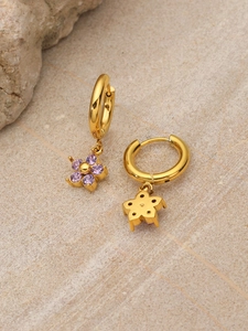 Detail of gold flower hoop earrings featuring purple crystals on a textured stone surface
