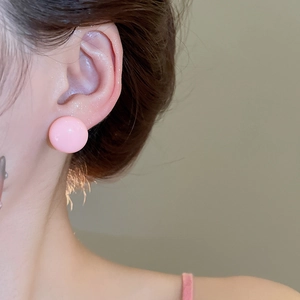 Close-up of minimalist pink round ball stud earrings worn on a female ear