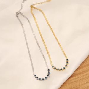 Flat lay of gold and silver snake chain necklaces with blue evil eye charms on silk