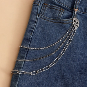 Detail of layered silver metal waist chain with skull pendant on dark blue jeans