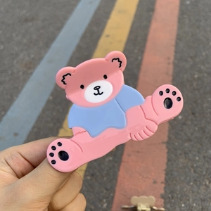 Détail de la pince à cheveux en forme d'ours rose et bleu tenue à la main à l'extérieur