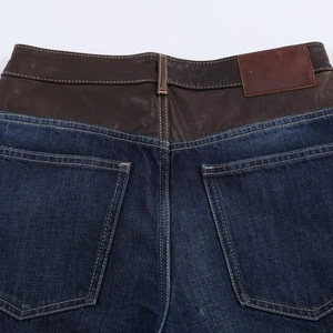 Détail d'un jean bleu foncé avec patchwork en cuir marron et coutures sur la poche arrière