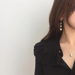 Detail of silver drop pendant necklace and triple bead earrings on a model in black