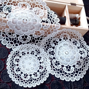 Close-up of white lace coasters featuring intricate floral cutout embroidery on dark wood