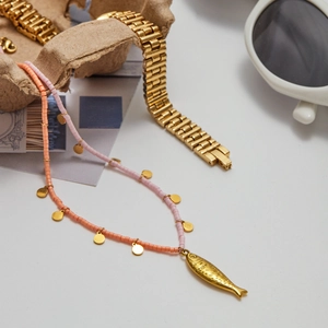 Detail showing a pink and orange beaded necklace with a gold fish pendant on a white table
