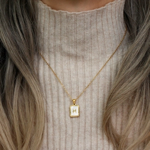 Detail of gold necklace with rectangular white shell pendant featuring Pisces zodiac symbol