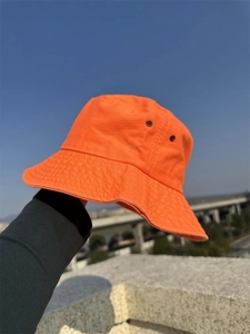 Detail view of orange cotton bucket hat with metal eyelets against blue sky background