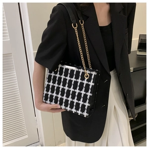 Détail de la texture en tweed à carreaux noir et blanc avec chaîne dorée sur le sac bandoulière