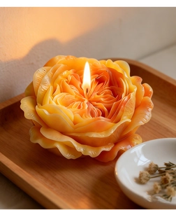 Detailed close-up of a lit orange gradient Austin rose scented candle on a wooden tray