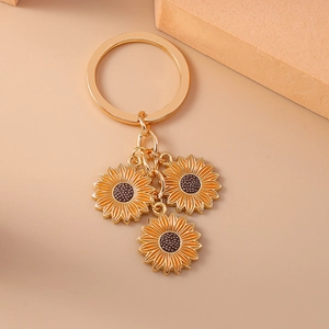 Close-up of golden keychain with three yellow sunflower enamel pendants on nude background