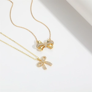 Detailed view of two gold bow necklaces featuring sparkling zircon stones on white background