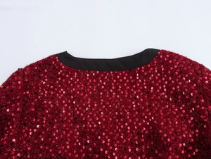Dettaglio dello scollo a V con paillettes rosse e bordo nero su una giacca in tweed
