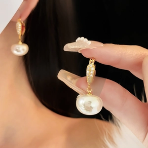 Dettaglio di orecchini placcati in oro con una perla bianca e piccoli diamanti brillanti