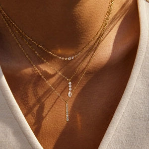 Gros plan sur un collier doré à trois rangs avec zircons en forme de poire et pendentif barre