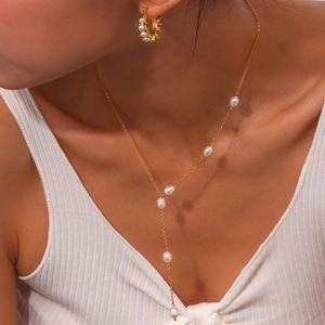 Close-up of elegant gold Y-shaped pearl necklace and matching hoop earrings on model