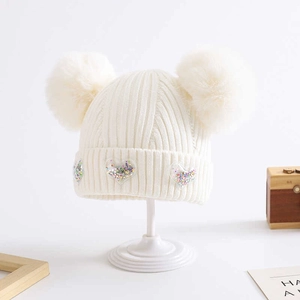 Close-up of white knitted baby hat with dual fluffy pom-poms and sequin heart charms