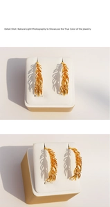 Detailed view of golden wheat ear earrings with intricate texture on a jewelry stand