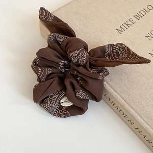 Detail of dark brown paisley scrunchie with bow accent resting on a vintage book