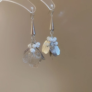 Close-up of hollow petal earrings with pearls hanging on a transparent acrylic stand