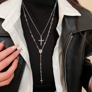 Detail of double-layer silver cross necklace with colored zircon stones and religious medal