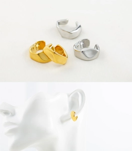 Detailed view of gold and silver irregular geometric ear cuffs on a textured white fabric