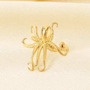 Detailed close-up of golden octopus-shaped stainless steel ring on beige textured fabric