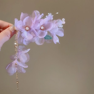 Détail d'une pince à cheveux fleur en tissu violet avec perle et pompons dorés