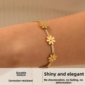 Detail of gold daisy flower charms on a flat blade chain bracelet worn on a wrist