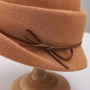 Detail of caramel knitted sun hat featuring a fine leather bow and intricate weave texture