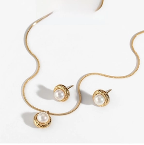 Macro detail of gold necklace and pearl earrings set with diamond-pattern metal finish