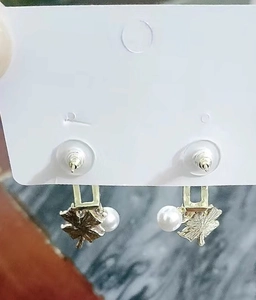 Close-up of pink clover-shaped earrings with gold leaves and white pearls details