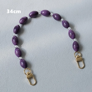 Close-up of a 34cm purple acrylic bead bag strap with lobster clasps on gray fabric