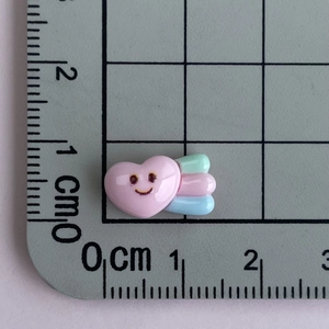 Mini resin heart charm with wings shown on a centimeter ruler for size reference