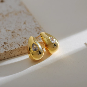 Macro shot of gold teardrop earrings featuring sparkling clear cubic zirconia on marble