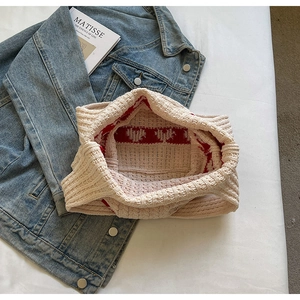 Primer plano de bolso de punto beige con corazones rojos sobre tela vaquera y revista