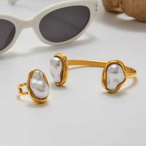 Ensemble bague et bracelet en acier doré avec perles baroques sur surface blanche