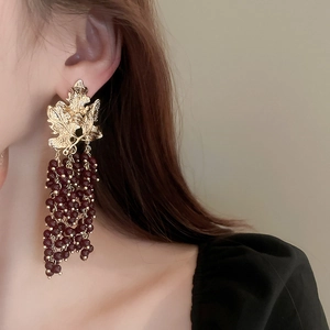 Macro detail of gold leaf stud and burgundy grape cluster tassel earrings on model