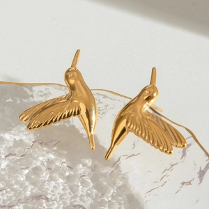 Minimalist gold hummingbird stud earrings in stainless steel on a decorative glass tray