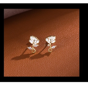 Macro detail of white enamel rose earrings with gold stems and sparkling zircon accents