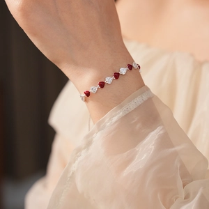 Close-up of a wrist wearing a heart bracelet with red enamel and white zircon stones
