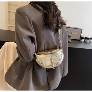 Detail of metallic gold half-moon crossbody bag with silver chain and fringe tassel